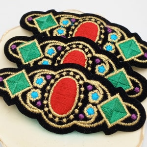 May include: Three black velvet embroidered patches with gold thread, featuring a large red oval gem, a green square gem, and smaller blue and purple gems.