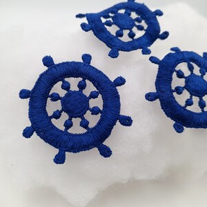 May include: Three blue fabric nautical wheel embellishments with a decorative design.