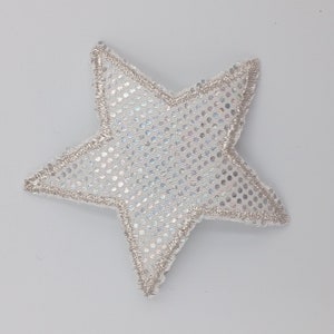 Puede incluir: Un parche en forma de estrella plateado con una tela blanca brillante y un borde bordado plateado.