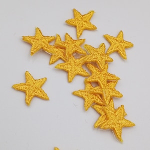 Puede incluir: Un conjunto de 10 estrellas de fieltro amarillo. Las estrellas están esparcidas sobre un fondo blanco.