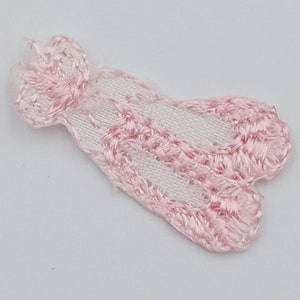 May include: Pink embroidered fabric applique with a white background. The applique is shaped like a butterfly with a scalloped edge.