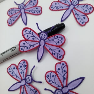 May include: Five purple and red embroidered butterfly iron-on patches with a happy face on each butterfly.