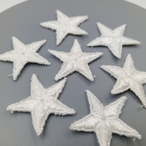 May include: Seven white felt star-shaped embellishments on a grey background.