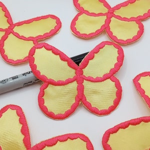 May include: Five yellow felt butterfly appliques with pink stitching around the edges. The butterflies are various sizes and are arranged on a white surface.