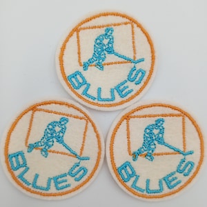 May include: Three white felt patches with an orange border. Each patch features a blue embroidered hockey player with a stick and the word "BLUES" in blue embroidery.