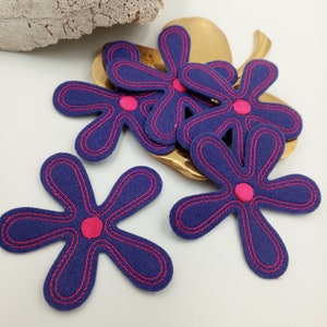 May include: Five purple felt flower shapes with pink centers. The flowers are sewn with a pink thread outline.