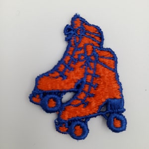 Op de afbeelding: Oranje en blauwe geborduurde patch van een paar rolschaatsen. De schaatsen hebben elk vier wielen.