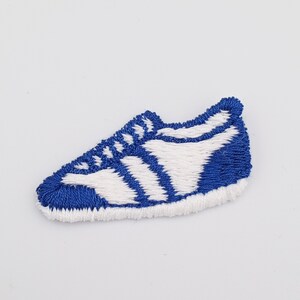 May include: Blue and white embroidered iron-on patch of a running shoe.