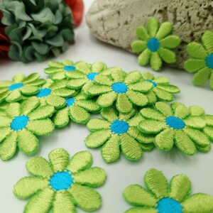 May include: A group of green felt flower embellishments with blue centers. The flowers are arranged in a pile on a white surface.