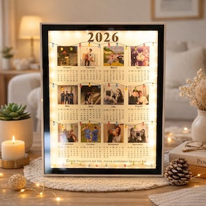 Könnte beinhalten: Ein beleuchteter Kalender für 2026 mit Fotos für jeden Monat. Der Kalender ist in Schwarz gerahmt und hat Lichterketten an den Rändern. Der Text "Crois toujours en toi, nous sommes là pour toi" steht unten.