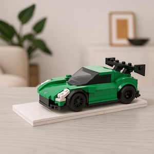 May include: A green toy sports car made of interlocking blocks. The car has black wheels, a rear spoiler, and white accents. It sits on a white base, with a blurred background of a room.