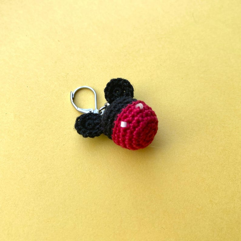May include: A small crocheted keychain featuring a red and black Mickey Mouse design. The keychain has a silver metal ring.
