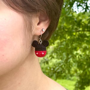 May include: Crocheted Mickey Mouse head earrings with red and white accents. The earrings are hanging from silver hooks.