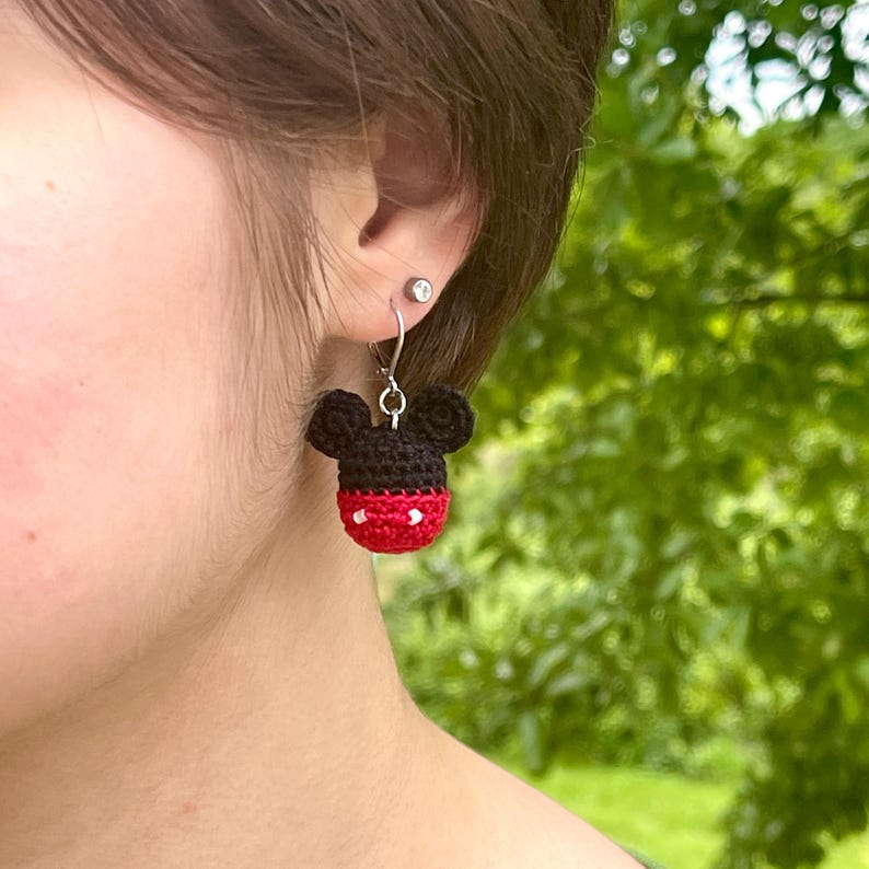 May include: Crocheted Mickey Mouse head earrings with red and white accents. The earrings are hanging from silver hooks.