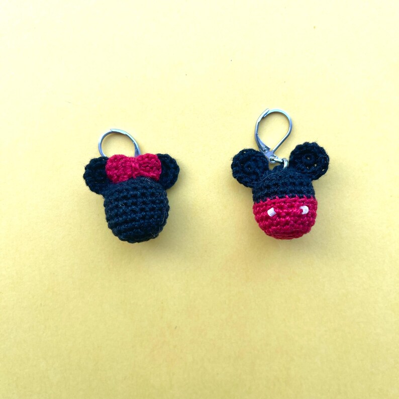 May include: Two crocheted Mickey Mouse keychains, one with a red bow and the other with a red nose and white eyes.