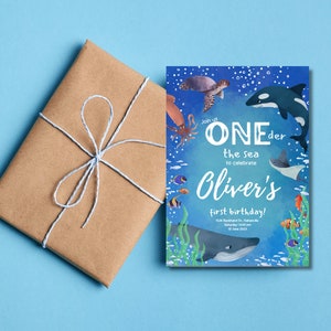Peut inclure: Une invitation aquarelle bleue et verte avec une baleine, une pieuvre, une tortue et d'autres cr&eacute;atures marines. Le texte indique "Rejoignez-nous ONEder la mer pour c&eacute;l&eacute;brer le premier anniversaire d'Oliver !"