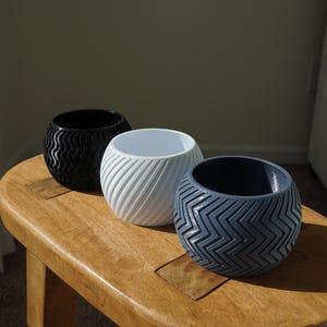 May include: Three round planters with different textured patterns. The planters are black, white, and blue. They are sitting on a wooden stool.