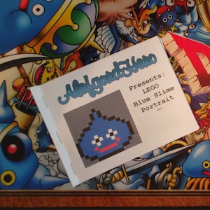 May include: A small booklet with a blue and white pixelated image of a blue slime monster. The booklet is titled "A Lego Hero Presents: LEGO Blue Slime Portrait 001".