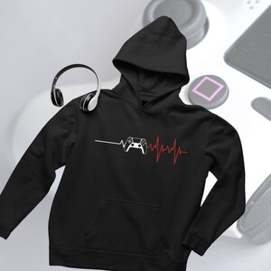 Op de afbeelding: Zwart hoodie met een witte videogamecontroller en een rode hartslaggrafiek. De tekst "Gaming" is op de hoodie gedrukt.