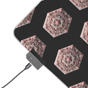 May include: Black mousepad with a repeating geometric pattern in shades of pink and white. The pattern features a series of interconnected, multi-faceted shapes. A black charging device with a power button is connected to the mousepad.