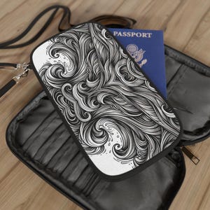 Peut inclure: Portefeuille de voyage noir et blanc avec un motif abstrait tourbillonnant. Le portefeuille est ouvert, révélant un passeport bleu. Il possède une sangle noire et une fermeture éclair. Le motif rappelle l'eau qui coule.