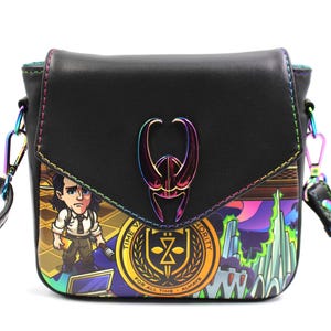 May include: Black crossbody bag with a flap closure and a rainbow-colored metal emblem. The bag features a colorful graphic print of a cartoon character and the text "TIME VARIANCE AUTHORITY". The strap and trim have a rainbow sheen.