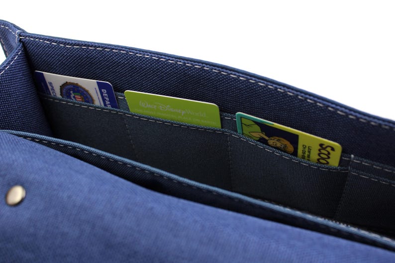 May include: A blue fabric wallet with multiple card slots. The wallet contains several cards, including a Walt Disney World card and a Scooby-Doo card. White stitching accents the edges of the wallet.