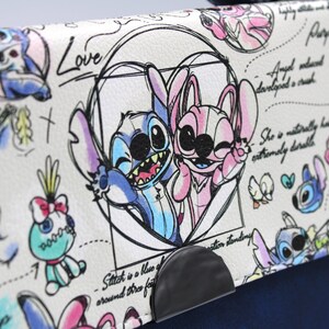 May include: A white handbag with a navy blue base and handle. The flap features a cartoon illustration of Stitch and Angel, with handwritten text and sketches. The design includes the words "Love" and "Angel".