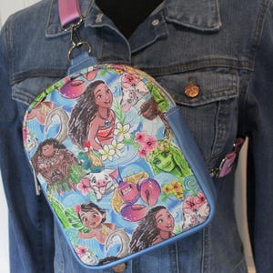 Puede incluir: Una bolsa bandolera azul y blanca con tem&aacute;tica de Moana. La bolsa presenta im&aacute;genes de Moana, Maui, Pua y otros personajes de la pel&iacute;cula. La bolsa tiene una correa ajustable rosa.