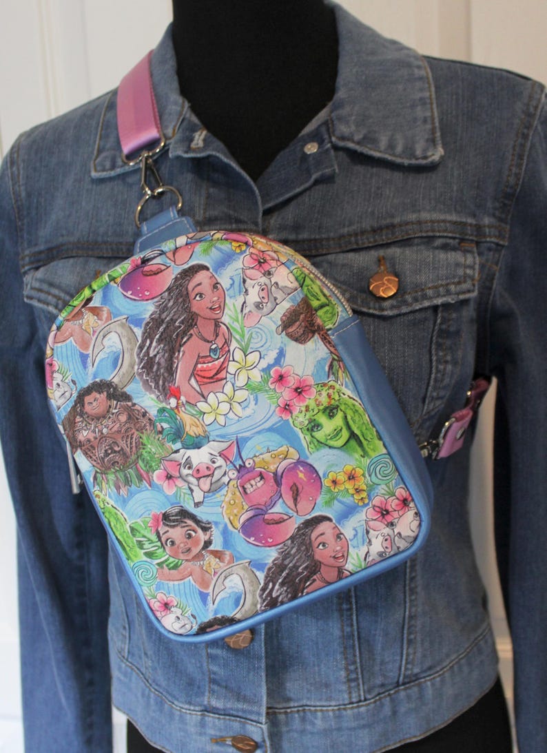 Puede incluir: Una bolsa bandolera azul y blanca con tem&aacute;tica de Moana. La bolsa presenta im&aacute;genes de Moana, Maui, Pua y otros personajes de la pel&iacute;cula. La bolsa tiene una correa ajustable rosa.