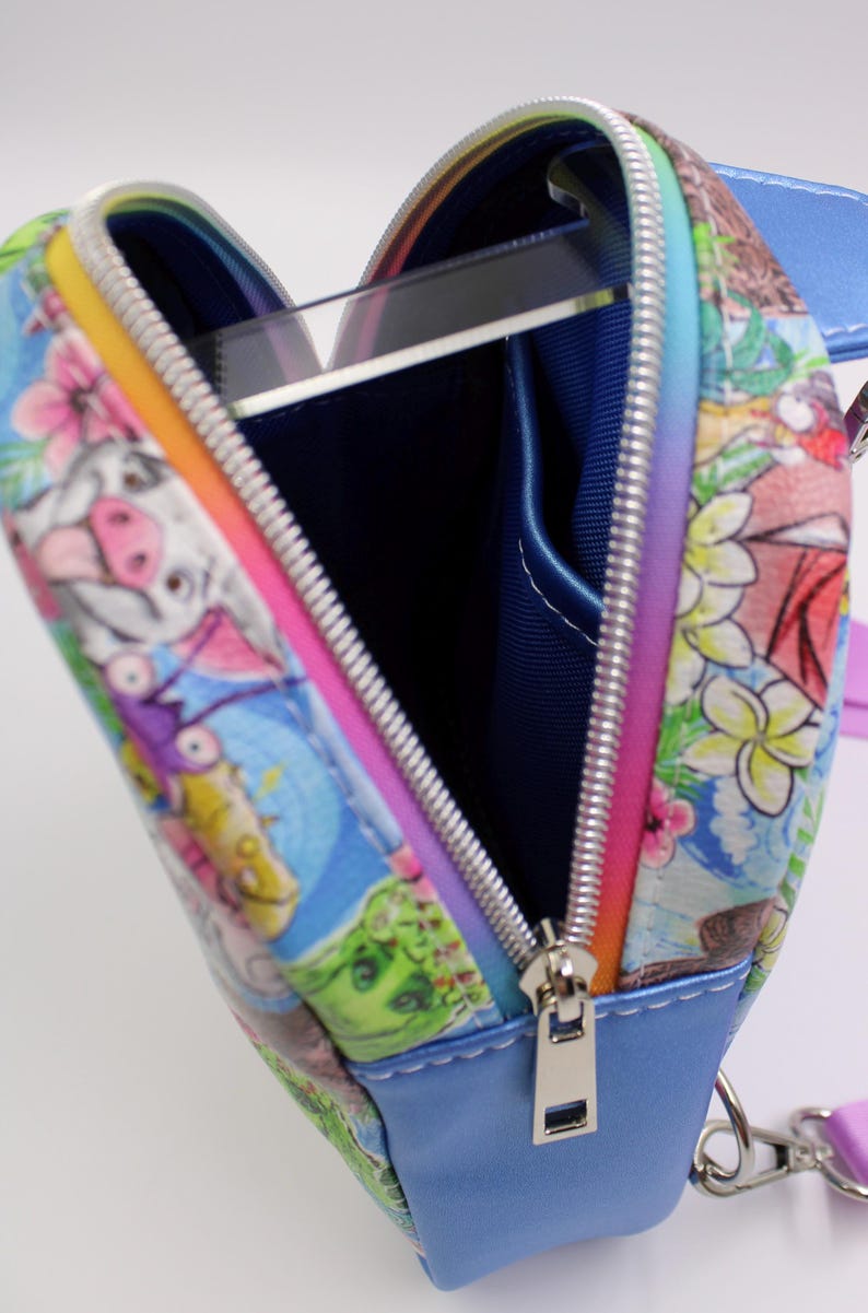 Puede incluir: Un peque&ntilde;o bolso azul en forma de coraz&oacute;n con cierre de cremallera. El bolso est&aacute; decorado con un estampado colorido de animales de dibujos animados y flores. El tirador de la cremallera es plateado.