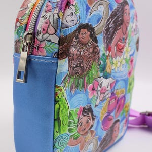 Puede incluir: Una peque&ntilde;a mochila azul con un estampado colorido con personajes de la pel&iacute;cula animada Moana. El estampado incluye a Moana, Maui, Pua el cerdo y otros personajes de la pel&iacute;cula. La mochila tiene una cremallera y una peque&ntilde;a correa.