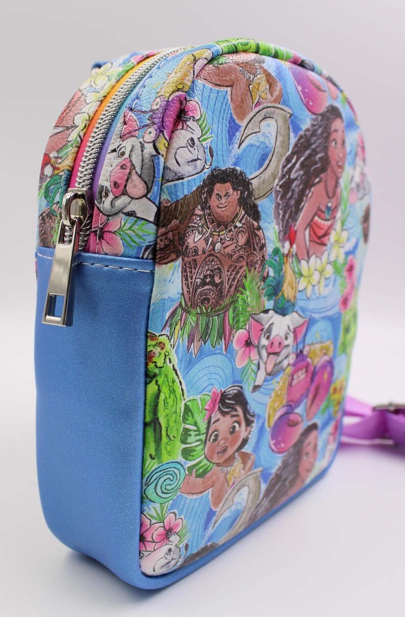Puede incluir: Una peque&ntilde;a mochila azul con un estampado colorido con personajes de la pel&iacute;cula animada Moana. El estampado incluye a Moana, Maui, Pua el cerdo y otros personajes de la pel&iacute;cula. La mochila tiene una cremallera y una peque&ntilde;a correa.