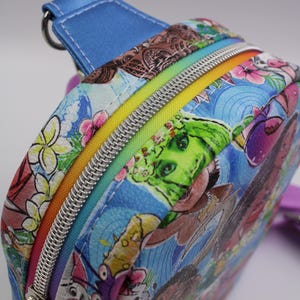 Puede incluir: Una peque&ntilde;a mochila azul con una cremallera arco&iacute;ris y un estampado colorido de personajes de dibujos animados y flores.