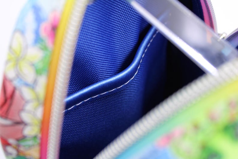 Puede incluir: Primer plano del interior de una peque&ntilde;a bolsa colorida. La bolsa tiene un forro de tela azul con un peque&ntilde;o bolsillo. El forro es visible a trav&eacute;s de la cremallera abierta.