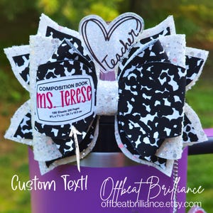 Può includere: Un grande fiocco decorativo per capelli con un design a quaderno. Il fiocco presenta una base glitterata bianca, dettagli a fantasia in bianco e nero e un abbellimento a forma di cuore con la scritta "Teacher". Il fiocco include il testo "Ms. Terese" e misure di 24,7 x 19,0 cm.