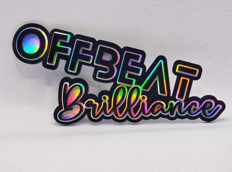 Puede incluir: Una pegatina negra e iridiscente con el texto "Offbeat Brilliance" en una fuente en negrita y estilizada.
