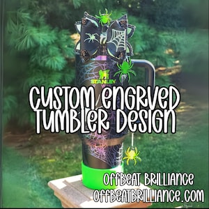 Puede incluir: Un vaso grabado personalizado en negro y verde con un diseño de telaraña. El vaso tiene una base verde y está decorado con arañas y lazos. El texto "CUSTOM ENGRAVED TUMBLER DESIGN" se muestra en el vaso.