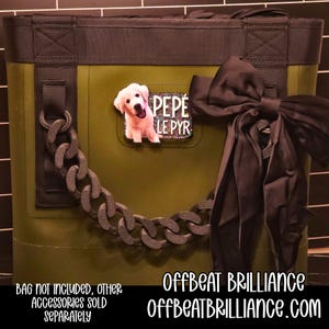 May include: An olive green tote bag with a black bow and a decorative chain. A small patch with a dog image and the text "PEPE LE PYR" is attached to the bag. The text "OFFBEAT BRILLIANCE" and "OFFBEATBRILLIANCE.COM" are also visible.