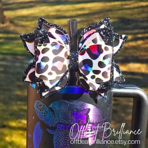 Puede incluir: Un lazo de estampado de leopardo blanco y negro con ribete de purpurina negra, sujeto a un vaso negro y morado con un diseño de tortuga marina y el texto "Offbeat Brilliance offbeatbrilliance.etsy.com".