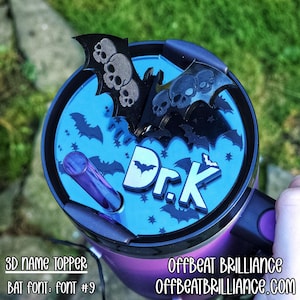 Może przedstawiać: Fioletowo-czarny kubek z niebieską pokrywką z motywami nietoperzy i czaszek. Na pokrywce widnieje napis "Dr. K" oraz słowa "3D NAME TOPPER" i "BAT FONT: FONT #9". Widoczna jest również strona internetowa "OFFBEATBRILLIANCE.COM".