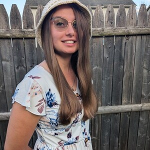May include: A woman with long brown hair wearing a white crocheted hat and a white dress with a floral pattern.