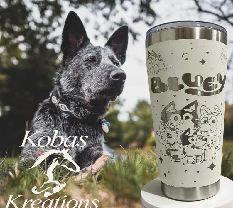 Puede incluir: Un vaso de acero inoxidable de color crema, con un dise&ntilde;o de dibujos animados de Bluey y la palabra "Bluey". El vaso est&aacute; decorado con estrellas y personajes de dibujos animados. Un perro est&aacute; en el fondo.