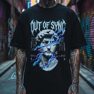 May include: A black short-sleeve t-shirt featuring a graphic print of a classical marble bust split by glowing blue and purple lightning bolts. The text "OUT OF SYNC" appears in a stylized metallic font above the bust, with circuit board patterns.