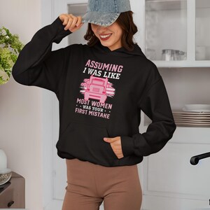 May include: Black hoodie with a pink graphic that says "Assuming I was like most women was your first mistake". The graphic also features a pink semi-truck.