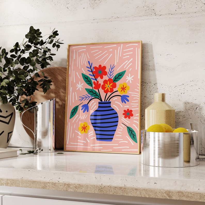 Puede incluir: Una impresi&oacute;n enmarcada en rosa y blanco de un jarr&oacute;n azul y blanco a rayas con flores rojas, naranjas y amarillas. El jarr&oacute;n est&aacute; lleno de flores y el fondo es un patr&oacute;n de rayas rosa y blanco.