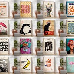 Pode incluir: Uma colagem de 16 impress&otilde;es de arte diferentes que apresentam v&aacute;rios designs, incluindo um flamingo, um sapo, um gato preto, um sol, um cupcake, uma banana e uma mulher com flores no cabelo. As impress&otilde;es est&atilde;o todas emolduradas em branco e s&atilde;o exibidas em uma parede branca.
