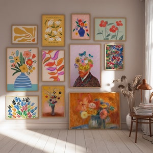 May include: A collection of framed art prints featuring floral and abstract designs. The prints showcase various styles, including colorful flower arrangements in vases, botanical illustrations, and a portrait with a floral head. The frames are a light wood color.