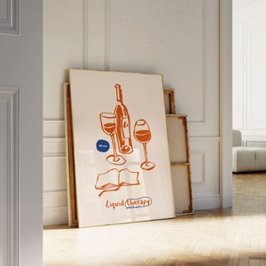 May include: A white framed print with a hand-drawn illustration of a wine bottle and two glasses. The text "Wine" is in a blue circle and the text "Liquid Therapy" is below the illustration.