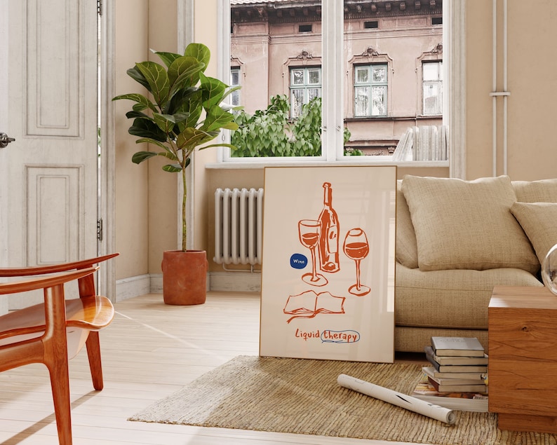 May include: A beige couch with a throw pillow and a stack of books on a wooden table. A framed illustration of a wine bottle and two glasses with the text "Liquid Therapy" is on the wall. A potted plant is in the corner of the room.